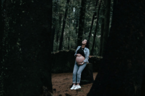 A pregnant Woman in jeans leaning against a tress after walking